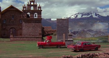 Movie still from “The Last Movie” (1971), directed by Dennis Hopper – A red truck and a red car parked in front of a church; Extreme Wide shot, Low angle