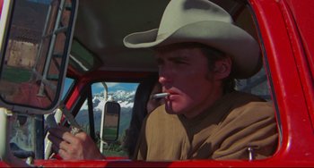 Movie still from “The Last Movie” (1971), directed by Dennis Hopper – A man wearing a cowboy hat smoking a cigarette while sitting in a car; Close Up shot, Low angle