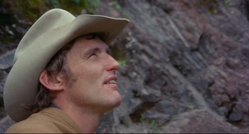 Movie still from “The Last Movie” (1971), directed by Dennis Hopper – A person wearing a cowboy hat near a rock wall; Close Up shot, Low angle