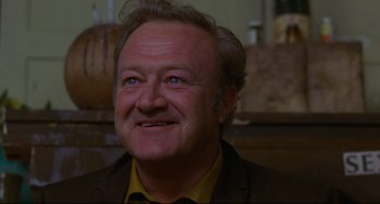 Movie still from “The Last Movie” (1971), directed by Dennis Hopper – An older man smiling for the camera in front of a wooden barrel; Close Up shot, Low angle