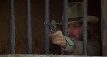 Movie still from “The Last Movie” (1971), directed by Dennis Hopper – A man with a gun in his hand is behind a fence; Close Up shot, Low angle