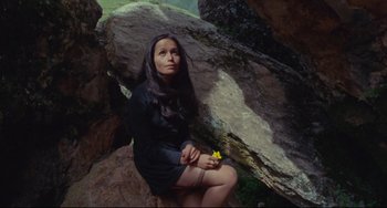 Movie still from “The Last Movie” (1971), directed by Dennis Hopper – A woman sitting on a rock with a flower in her hand; Medium shot, High angle