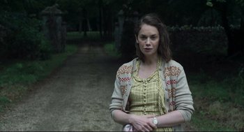 Movie still from “The Little Stranger” (2018), directed by Lenny Abrahamson – A woman standing on a dirt path in a wooded area; Medium shot, Over the shoulder angle