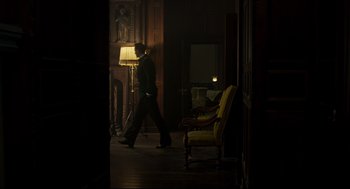 Movie still from “The Little Stranger” (2018), directed by Lenny Abrahamson – A man walking in a dark room with a lamp; Wide shot, Low angle
