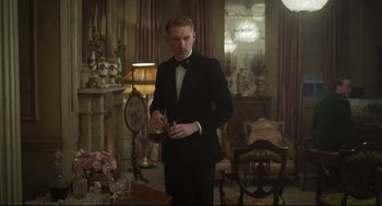 Movie still from “The Little Stranger” (2018), directed by Lenny Abrahamson – A man in a tuxedo standing in front of a table; Medium shot, Over the shoulder angle