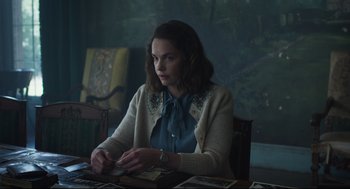 Movie still from “The Little Stranger” (2018), directed by Lenny Abrahamson – A woman sitting at a table looking at photos; Medium shot, Over the shoulder angle