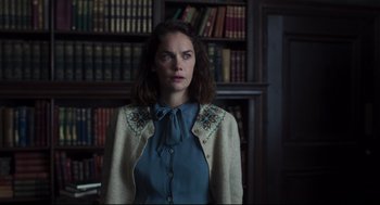 Movie still from “The Little Stranger” (2018), directed by Lenny Abrahamson – A woman standing in front of bookshelves in a library; Medium shot, Low angle