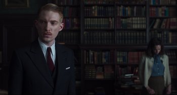 Movie still from “The Little Stranger” (2018), directed by Lenny Abrahamson – A man in a suit standing in front of bookshelves; Medium shot, Low angle