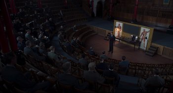 Movie still from “The Little Stranger” (2018), directed by Lenny Abrahamson – An audience is sitting in the auditorium and watching a presentation on a large screen; Extreme Wide shot, High angle