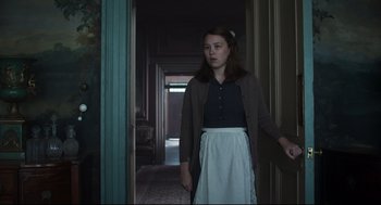 Movie still from “The Little Stranger” (2018), directed by Lenny Abrahamson – A woman standing in a hallway wearing a skirt; Medium shot, Low angle