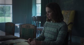 Movie still from “The Little Stranger” (2018), directed by Lenny Abrahamson – A woman sitting at a table in a dark room; Medium shot, Over the shoulder angle