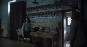 Movie still from “The Little Stranger” (2018), directed by Lenny Abrahamson – A woman standing in front of a table in a kitchen; Wide shot, High angle