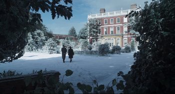 Movie still from “The Little Stranger” (2018), directed by Lenny Abrahamson – Two people walking in the snow near a large building; Extreme Wide shot, High angle