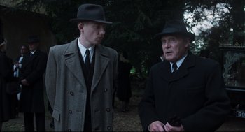 Movie still from “The Little Stranger” (2018), directed by Lenny Abrahamson – Two men in suits and hats standing next to each other in a forest; Medium shot, Low angle