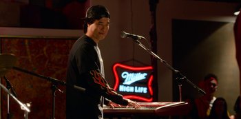 Movie still from “Always Be My Maybe” (2019), directed by Nahnatchka Khan – A young man playing a keyboard in front of a microphone; Medium shot, Over the shoulder angle