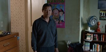 Movie still from “Always Be My Maybe” (2019), directed by Nahnatchka Khan – An older man standing in front of a poster; Medium shot, Over the shoulder angle
