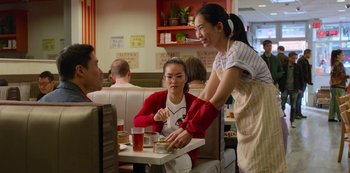Movie still from “Always Be My Maybe” (2019), directed by Nahnatchka Khan – A woman serving food at a table in a restaurant; Medium shot, Over the shoulder angle