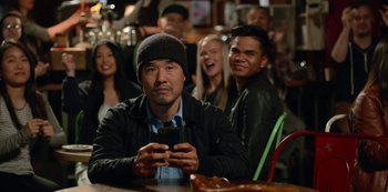 Movie still from “Always Be My Maybe” (2019), directed by Nahnatchka Khan – A man sitting at a table looking at a cell phone; Medium shot, Over the shoulder angle