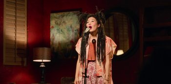 Movie still from “Always Be My Maybe” (2019), directed by Nahnatchka Khan – A woman with dreads standing in front of a microphone; Medium shot, High angle