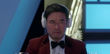 Movie still from “Always Be My Maybe” (2019), directed by Nahnatchka Khan – A man in a red jacket and bow tie wearing white headphones; Close Up shot, Over the shoulder angle