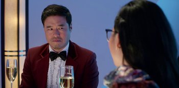 Movie still from “Always Be My Maybe” (2019), directed by Nahnatchka Khan – A man in a red jacket is sitting at a table with a glass of champagne; Close Up shot, Over the shoulder angle