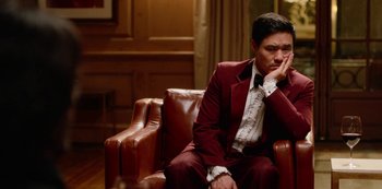 Movie still from “Always Be My Maybe” (2019), directed by Nahnatchka Khan – A man in a red suit sitting on a brown leather chair; Medium shot, High angle