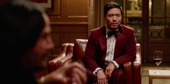 Movie still from “Always Be My Maybe” (2019), directed by Nahnatchka Khan – A man sitting on a chair wearing a red suit and a bow tie; Medium shot, Over the shoulder angle