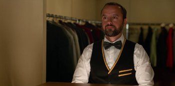Movie still from “Always Be My Maybe” (2019), directed by Nahnatchka Khan – A man wearing a vest and bow tie in front of a row of suits; Medium shot, Over the shoulder angle