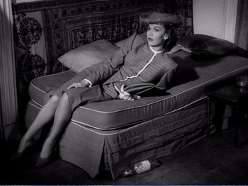 Movie still from “The Lost Weekend” (1945), directed by Billy Wilder – A woman sitting on top of a bed next to a bottle of beer; Wide shot, High angle