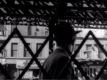 Movie still from “The Lost Weekend” (1945), directed by Billy Wilder – A man in a baseball cap is standing behind a fence; Wide shot, Over the shoulder angle