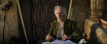 Movie still from “The Man Who Killed Don Quixote” (2018), directed by Terry Gilliam – An older man sitting at a table with a cup of coffee; Medium shot, Over the shoulder angle
