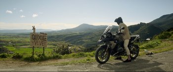 Movie still from “The Man Who Killed Don Quixote” (2018), directed by Terry Gilliam – A person on a motorcycle on the side of a road; Wide shot, Low angle