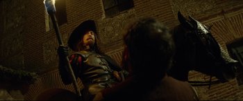 Movie still from “The Man Who Killed Don Quixote” (2018), directed by Terry Gilliam – A man dressed as a pirate sitting next to a brick building; Medium shot, Over the shoulder angle