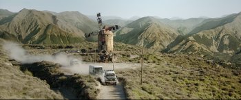 Movie still from “The Man Who Killed Don Quixote” (2018), directed by Terry Gilliam – A truck and a van driving down a dirt road near a windmill; Extreme Wide shot, Low angle