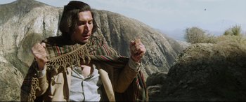 Movie still from “The Man Who Killed Don Quixote” (2018), directed by Terry Gilliam – A man holding a piece of food while standing on top of a mountain; Medium shot, Low angle