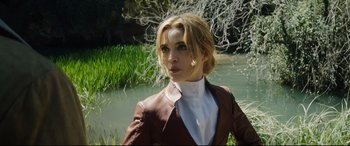 Movie still from “The Man Who Killed Don Quixote” (2018), directed by Terry Gilliam – A woman wearing a brown jacket standing next to a body of water; Medium shot, Low angle