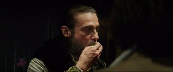 Movie still from “The Man Who Killed Don Quixote” (2018), directed by Terry Gilliam – A man with a goatee is eating a piece of food; Close Up shot, Over the shoulder angle