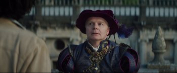Movie still from “The Man Who Killed Don Quixote” (2018), directed by Terry Gilliam – A man wearing a purple hat and a chain around his neck; Close Up shot, Over the shoulder angle