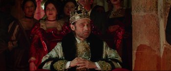 Movie still from “The Man Who Killed Don Quixote” (2018), directed by Terry Gilliam – A man wearing a crown sitting in front of other people; Medium shot, Low angle