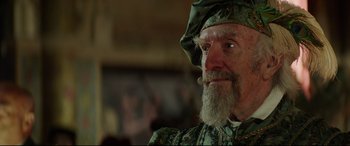 Movie still from “The Man Who Killed Don Quixote” (2018), directed by Terry Gilliam – An old man with a long beard wearing a green hat; Close Up shot, Over the shoulder angle