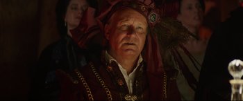 Movie still from “The Man Who Killed Don Quixote” (2018), directed by Terry Gilliam – An older man wearing a red and gold headdress; Close Up shot, Over the shoulder angle