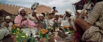 Movie still from “The Man Who Would Be King” (1975), directed by John Huston – A group of men sitting around a table with flowers; Wide shot, Low angle