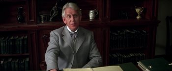 Movie still from “The Man Who Would Be King” (1975), directed by John Huston – An older man sitting at a desk in a suit; Close Up shot, Over the shoulder angle