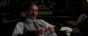 Movie still from “The Man Who Would Be King” (1975), directed by John Huston – A man in a suit and tie holding a pair of glasses; Close Up shot, High angle