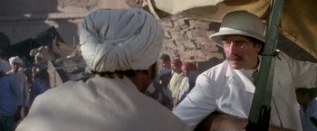 Movie still from “The Man Who Would Be King” (1975), directed by John Huston – A group of men standing next to each other in front of a brick wall; Medium shot, Over the shoulder angle