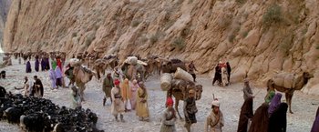 Movie still from “The Man Who Would Be King” (1975), directed by John Huston – A group of people walking down a dirt road; Extreme Wide shot, High angle