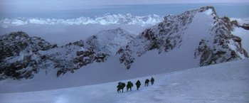 Movie still from “The Man Who Would Be King” (1975), directed by John Huston – A group of people riding horses on top of a snow covered slope; Extreme Wide shot, High angle