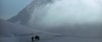 Movie still from “The Man Who Would Be King” (1975), directed by John Huston – A man standing next to two horses on a snowy hill; Extreme Wide shot, High angle