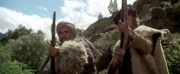 Movie still from “The Man Who Would Be King” (1975), directed by John Huston – A man with a beard holding a gun and a rifle; Medium shot, Low angle