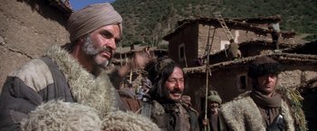 Movie still from “The Man Who Would Be King” (1975), directed by John Huston – A group of men standing next to each other in a village; Medium shot, Low angle